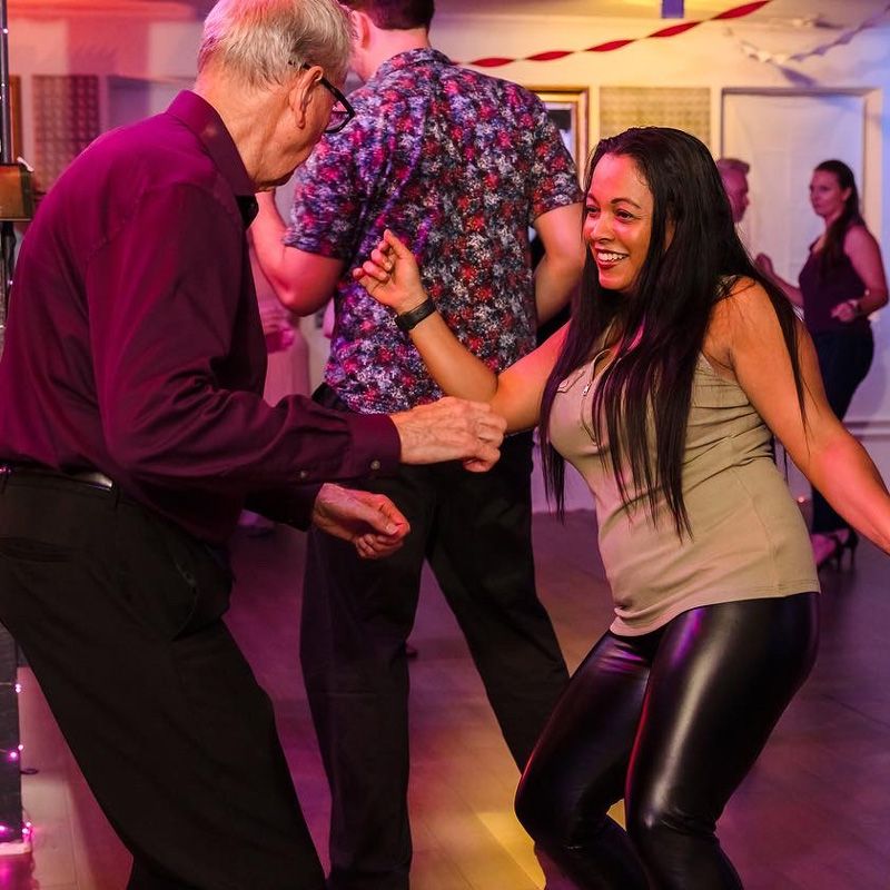 A joyful pair dancing at a social event under vibrant lights, celebrating in Gainesville, FL