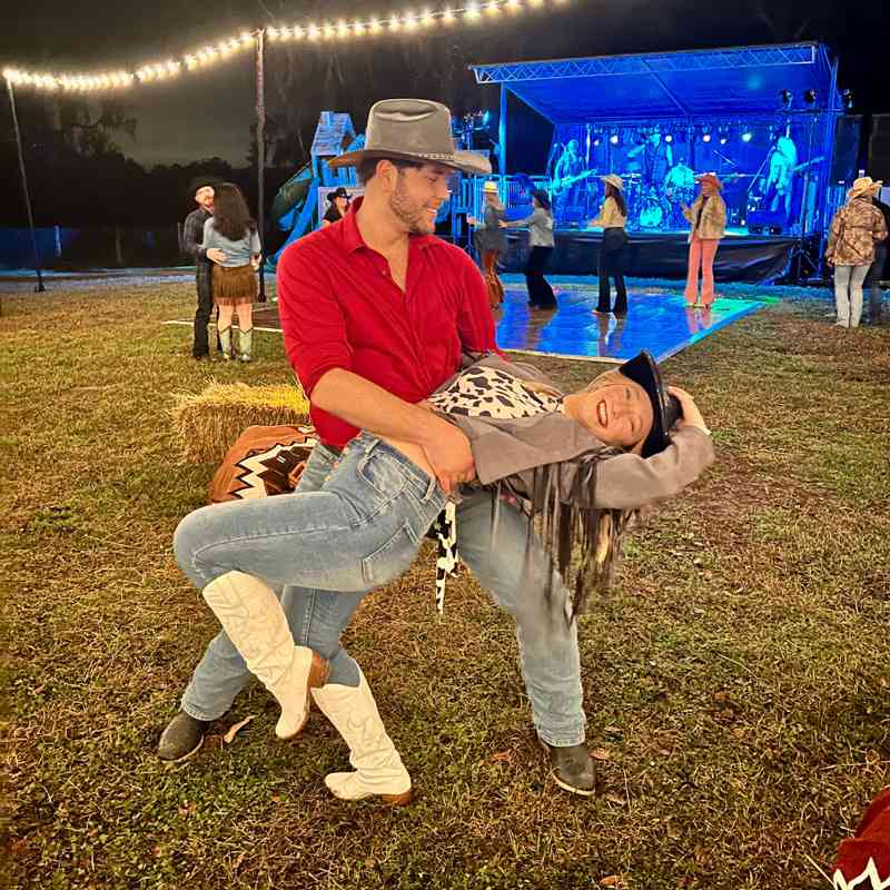A couple swing dancing at a country-western event with a live band & string lights in Gainesville